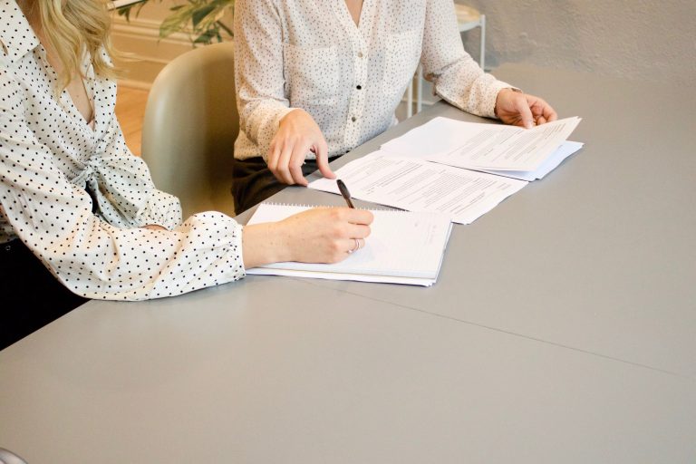 Two woman with papers in an office with one making notes