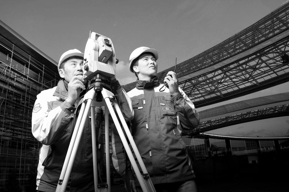 Black and white of two hard-hatted surveyors with measuring equipment