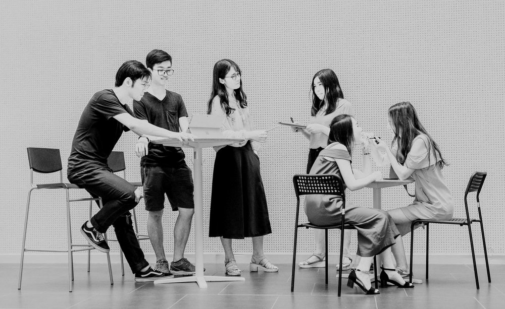 Black and white of seating and standing young men and woman in a work environment