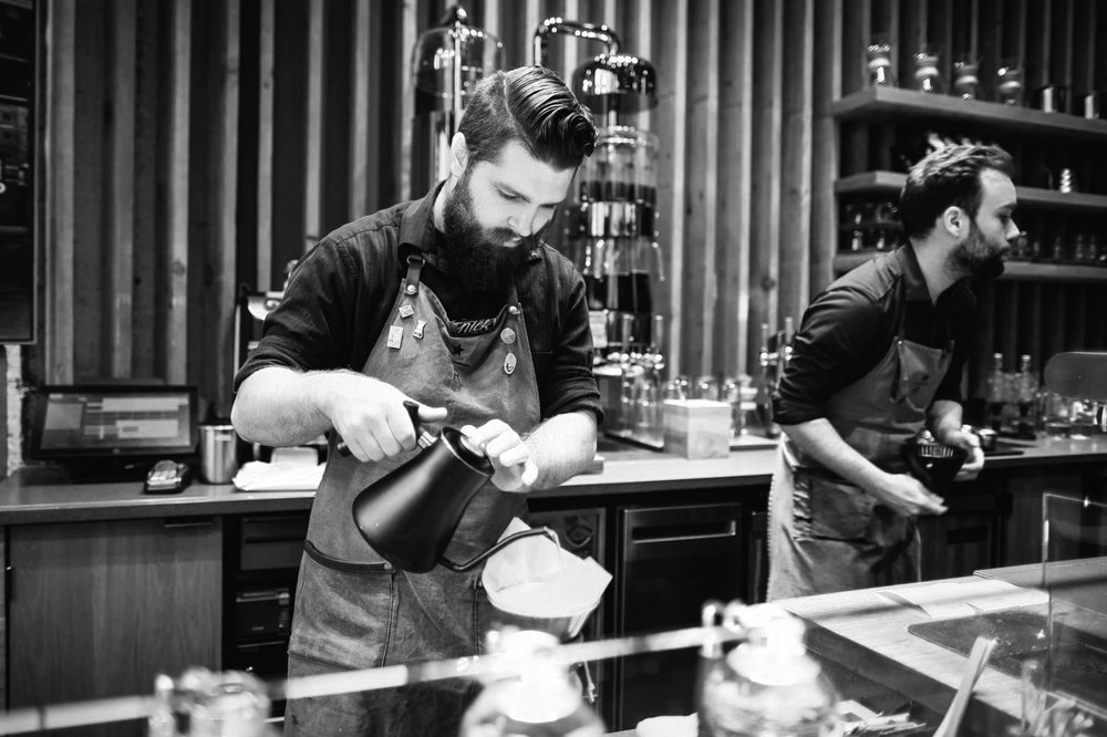 Black and white of a man pouring liquid in a coffee shop