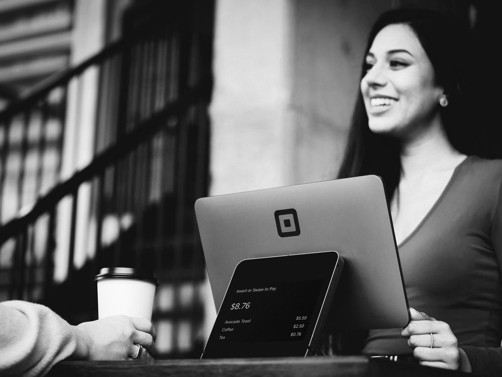 Black and white off a smiling woman holding a laptop beside a tablet with financial figures